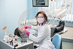 Female dentist with dental tools - mirror and probe treating patient teeth at dental clinic office