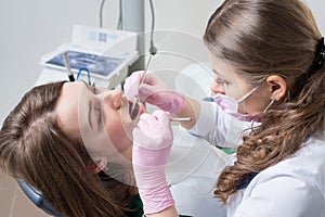 Female dentist with dental tools - mirror and probe treating patient teeth at dental clinic office. Dental equipment