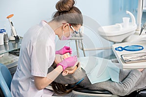 Female dentist with dental tools - mirror and probe treating patient teeth at dental clinic office