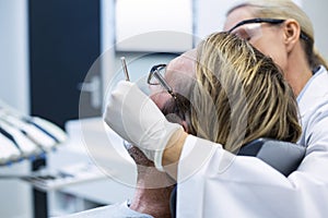 Female dentist examining male patient with tools