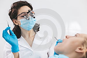 Female dentist examining patient's mouth using stomatological binoculars