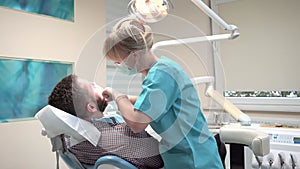 Female dentist examining teeth of male patient looks to the camera.