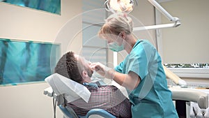 Female dentist examining teeth of male patient. Slider shot, right.