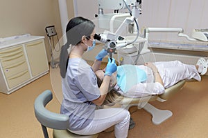 Female dentist examining a woman looking at her teeth with a professional microscope in a surgical dental office