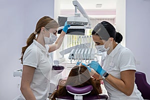 female dentist and a female assistant in a special uniform treat the teeth of a female patient.