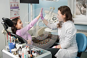 Female dentist and girl patient satisfied after treating teeth at dental clinic office, smiling and doing high-five