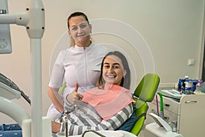 Female dentist with happy satisfied woman client giving thumbs up after good service