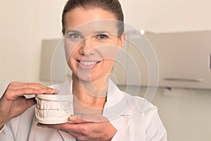 Female dentist holding white dentures at clinic