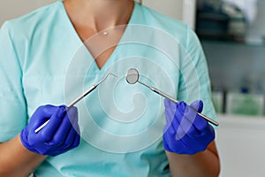 Female dentist holds professional dentist tools in the dental office, mirror and curved tweezers