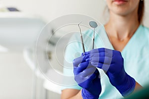 Female dentist holds professional dentist tools in the dental office, mirror and curved tweezers