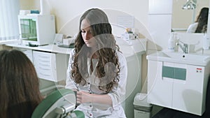 A female dentist with long dark curly hair takes in her patient`s office. The doctor prepares for a dental checkup, puts