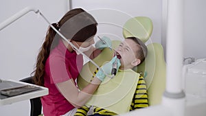 Female dentist making careful brushing child's teeth with dental tools in clinic