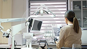 A female dentist in a mask looks at an x-ray image of a patient while standing in her office.