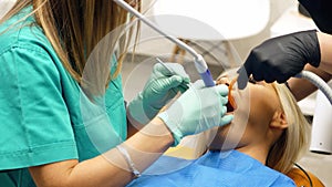 A female dentist removing dental plaque from the teeth of a young woman