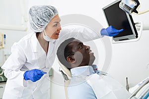 Female dentist showing smiling patient x-ray of teeth after dental treatments