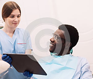 Female dentist showing teeth x-ray to afro male at dental clinic office.