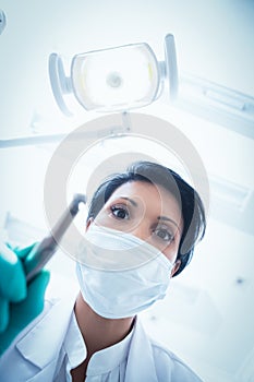 Female dentist in surgical mask holding dental drill