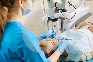 Female dentist treating caries using microscope at the dentist office