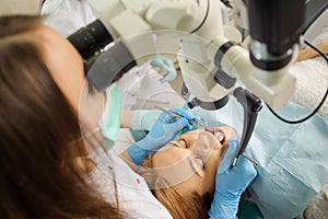 Female dentist treating caries using microscope at the dentist office