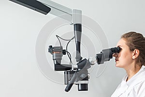 Female dentist using dental microscope treating patient teeth at dental clinic office. Medicine, dentistry and health