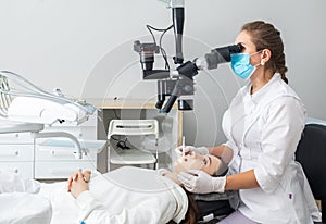 Female dentist using dental microscope treating patient teeth at dental clinic office. Medicine, dentistry and health