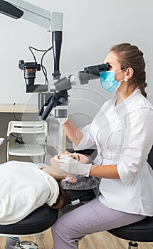 Female dentist using dental microscope treating patient teeth at dental clinic office. Medicine, dentistry and health