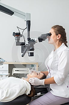 Female dentist using dental microscope treating patient teeth at dental clinic office. Medicine, dentistry and health