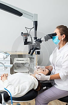 Female dentist using dental microscope treating patient teeth at dental clinic office. Medicine, dentistry and health