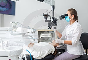 Female dentist using dental microscope treating patient teeth at dental clinic office. Medicine, dentistry and health