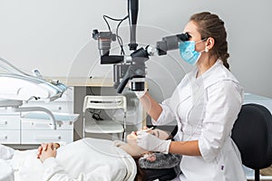 Female dentist using dental microscope treating patient teeth at dental clinic office. Medicine, dentistry and health