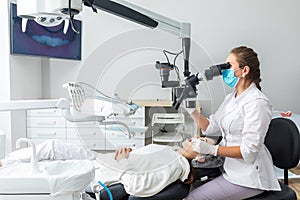 Female dentist using dental microscope treating patient teeth at dental clinic office. Medicine, dentistry and health