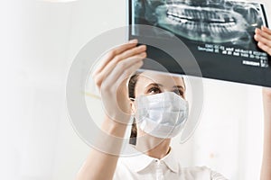 Female dentist wearing mask while examining x-ray at dental clinic