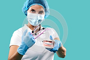 Female dentist wearing protective medical mask and uniform holds model jaws and dental tools between her fingers and looks at the