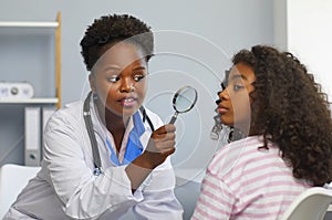 Female dermatologist examines teenage girl's face with magnifying glass for moles and redness.
