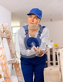 Female designer in blue overalls making checklist while planning building overhaul