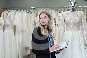 female designer or seller making notes near dress in wedding fashion shop