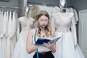 female designer or seller making notes near dress in wedding fashion shop
