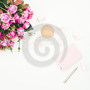 Female desk with pink roses bouquet, pink diary, coffee mug and marshmallows on white background. Flat lay. Top view feminine back