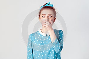 Female in despair and shock. Portrait of young desperate redhead girl in blue dress looking panic, covered her mouth by hand.