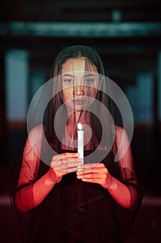 a female devil worshiper with a transparent veil is performing a spooky ritual by holding a candle in her hand photo