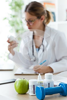 Female dietician holding a nutritional supplement while writing the properties in the consultation.