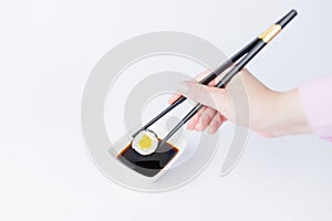 Female dipping tasty sushi makaki or uramaki with chopsticks into bowl with soy sauce on table. Space for copy