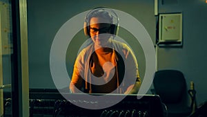 A female DJ with headphones in a technical room conducts a disco at a mixing console in the light of a disco