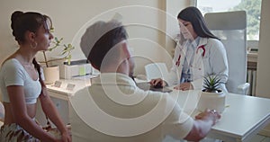 Female doctor advises a couple in a clinic, discussing medical results and treatment options for their health problems.