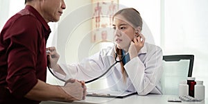 Female doctor asian cardiologist examining senior male cardiac patient listening checking heartbeat using stethoscope at