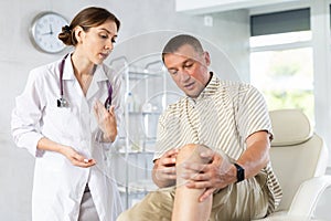 Female doctor ask and attentively listen to man patients complaints about pain and stiffness in knee photo