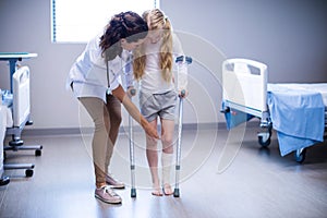 Female doctor assisting girl to walk with crutches in ward