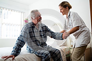 Female doctor assisting man in standing at nursing home