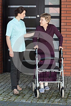 Female doctor assisting old woman with walker