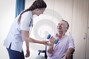 Female doctor assisting senior man in lifting dumbbell